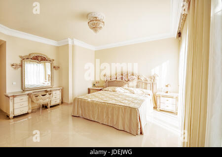 Luxuriöses Schlafzimmer in Pastellfarben im neoklassizistischen Stil, mit einem großen Bett und einem Frisiertisch mit Marmorböden ausgestattet. Stockfoto