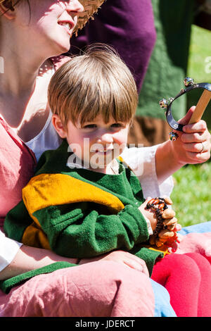 Mittelalterliche Re-enactment Veranstaltung. Kaukasier Kind, junge, blonde, sitzen auf den Müttern einhüllen und lächelnd direkt auf Viewer. In mittelalterliche Kleidung angezogen. Stockfoto