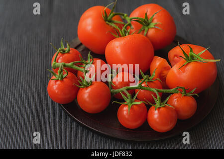 Nahaufnahme von frischen roten reif Organik Tomaten mit Wasser fällt auf Zweigen, dunkle Leinen-Serviette. Selektiven Fokus. Ansicht von oben. Konzept der vegetarische und gesunde Ernährung Stockfoto