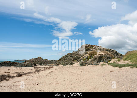 Vulkangestein, blauer Himmel und Wolken am Strand Newborough, Anglesey, Gwynedd, Wales, Vereinigtes Königreich Stockfoto