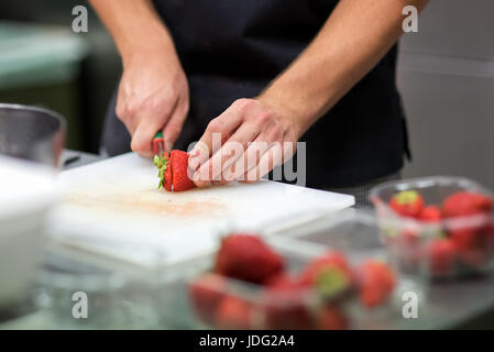 Koch bereitet frische tropische Früchte Salat schneiden Reife rote Erdbeeren auf ein Schneidebrett in einer Großküche in einem flachen Winkel Nahaufnahme auf Hallo Stockfoto