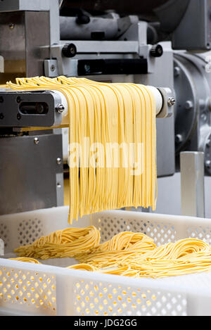 Frische italienische Spaghetti Nudeln mit einer Nahaufnahme der ungekochten Bänder zu machen, wie sie die automatische Schneidemaschine Stockfoto
