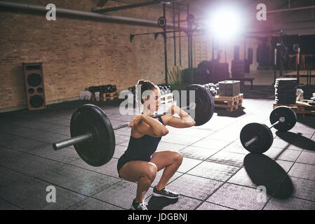Junge Frau hocken halten schwere Langhantel auf Schultern in leichte Fitness-Studio. Stockfoto