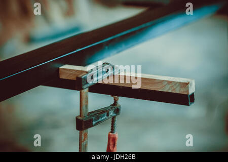 Handwerker mit Klammern fixieren zwei Stücke aus Holz und Eisen. Der Prozess der Herstellung Schreibtisch, Möbel. Soft-Fokus. Flachen DOF. Stockfoto