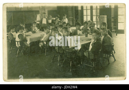 Postkarte des frühen 1900 von Säuglingen aus Kindergarten oder Grundschule Alter Kinder sitzen an Tischen essen Frühstück, Abendessen oder einen Snack, tragen Servietten, Großbritannien Stockfoto