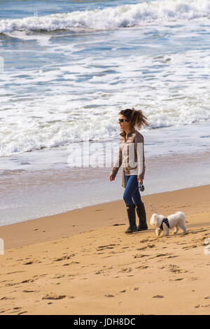 Frau zu Fuß Hund entlang der Meeresküste in Bournemouth Strand Meer in Bournemouth, Dorset im April Stockfoto