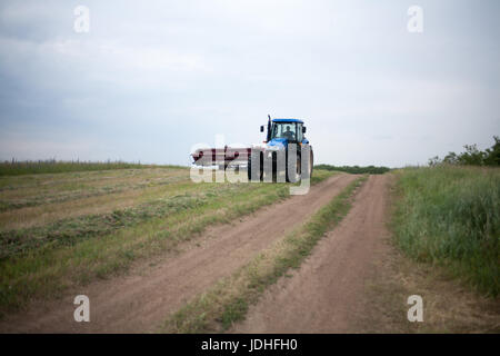 Traktor mit Mähwerk Rasenmähen im Sommer-Sommer-Bereich. Weide Mähen mit blauen Traktor und Mähwerk Stockfoto