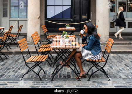 Eine junge schwarze Frau Kaffeetrinken am Bürgersteig Café, Covent Garden, London, UK Stockfoto