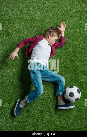 Draufsicht eines jungen mit Fußball auf dem grünen Rasen liegend Stockfoto
