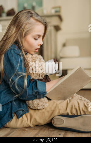 Seitenansicht von kleinen Mädchen mit Teddybär Lesebuch, Kinder Bildung Konzept Stockfoto