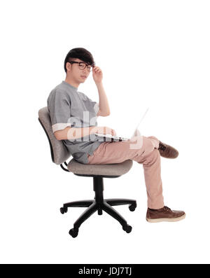Ein junger Mann sitzt und arbeitet mit seinem Laptop schaut in die Kamera, mit Brille, für weißen Hintergrund isoliert. Stockfoto