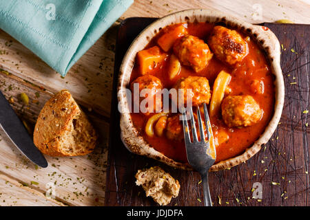 High-Angle Shot eine Steingut-Schale mit typisch spanischen Albondigas con Sepia, Frikadellen mit Tintenfisch, ein Stück Brot, eine Gabel und ein Messer auf ein Stockfoto