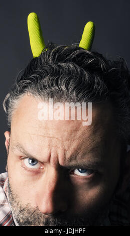 Verärgerter Mann mit Grinsen auf seinem schönen bärtigen Gesicht Hand mit Rock Metal Geste auf einem dunklen Hintergrund Stockfoto