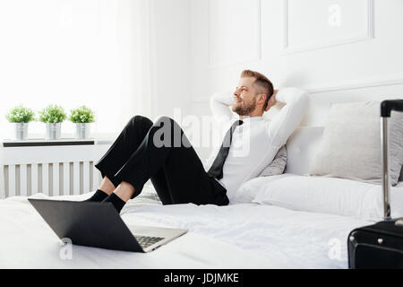 Entspannen Sie sich auf Bett in seinem Hotelzimmer junger Geschäftsmann Stockfoto