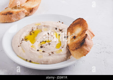 Hausgemachter Hummus mit Kichererbsen, geröstetem Knoblauch, Pfeffer und Tahini auf weißen Teller Stockfoto