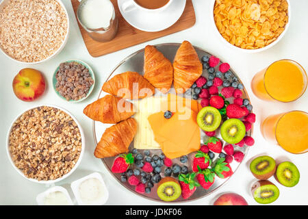Obenliegende Foto von einem kontinentalen Frühstück auf weißem Hintergrund. Eine Auswahl an Croissants, Käse, frisches Obst, Orangensaft, Müsli-Schalen, cof Stockfoto