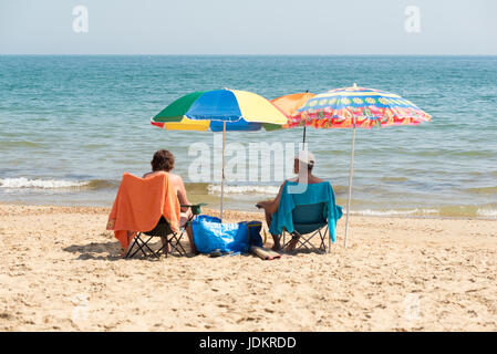 Boscombe Beach, Bournemouth, Dorset, Großbritannien, 20.. Juni 2017. Ein Paar, das während der längsten Juni-Hitzewelle seit über 20 Jahren im Schatten ihrer bunten Regenschirme sitzt. Stockfoto