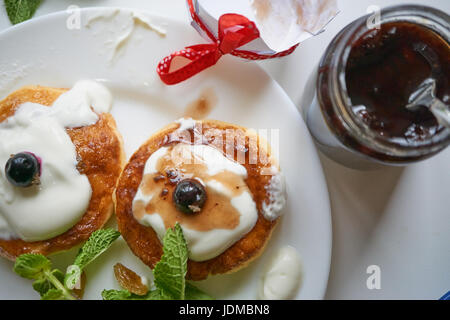 Quark Quark Pfannkuchen auf weißen Teller mit Rosinen, Minze und Johannisbeere Beeren. Glas mit Marmelade geöffnet. Nahaufnahme Makroaufnahme von oben. hohen Winkel Stockfoto