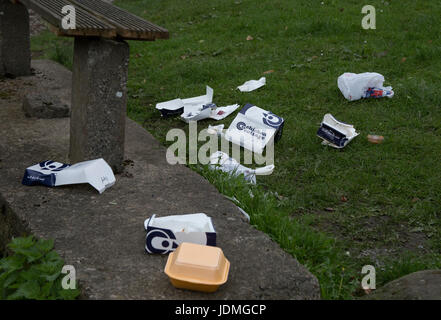 Wurf ist auf dem Rasen um eine Bank übersät. Stockfoto