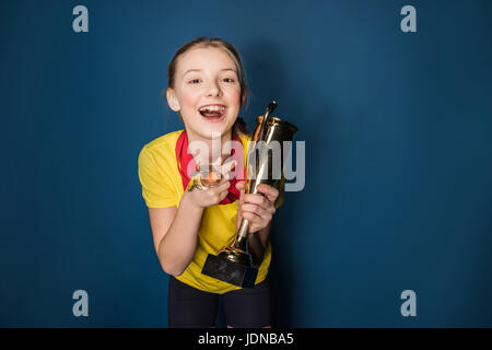 aufgeregt Mädchen mit Medaillen und Trophäen Tasse isoliert auf blau Stockfoto