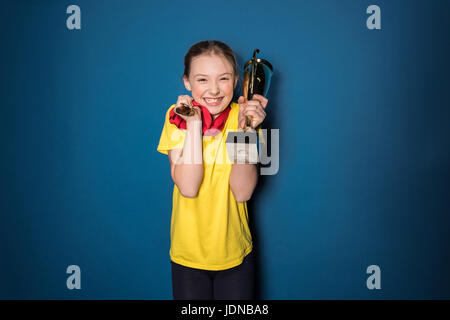 aufgeregt Mädchen mit Medaillen und Trophäen Tasse isoliert auf blau Stockfoto