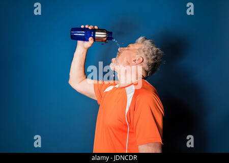 Sportlicher reifen Mann in Sportbekleidung gießt Wasser aus Sportflasche auf Gesicht Stockfoto