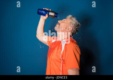 Sportlicher reifen Mann in Sportbekleidung gießt Wasser aus Sportflasche auf Gesicht Stockfoto