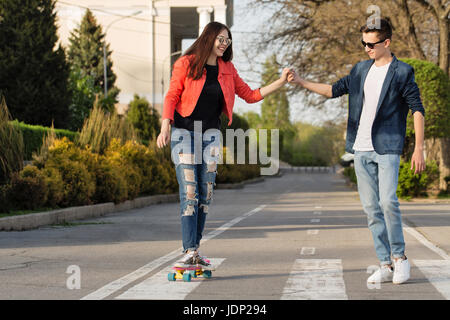 Verliebte Teenager. Der Kerl unterrichtet seine Freundin Skateboard. Datum der Hipster. Hand in hand. Romance erste Liebe. Stockfoto