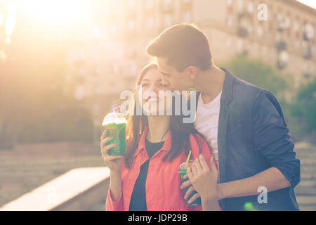 Jugendliche trinken Obst frisch aus Gläsern. Er umarmt und küsst sie. Paar in der Liebe. Romantik der ersten Liebe. Stockfoto