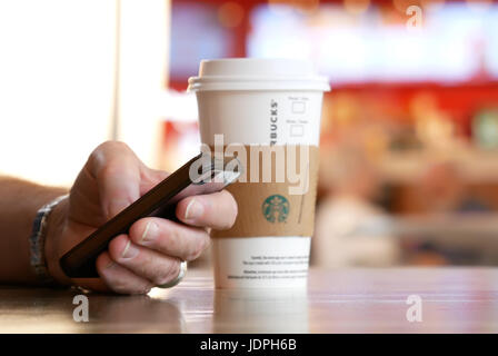 Burnaby, BC, Kanada - 4. Mai 2017: Mann lesen Nachricht auf seinem Handy und trinken Starbucks heißen Getränk Kaffee mit blur Bewegung Menschen am Food-court Stockfoto