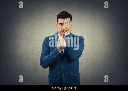 Porträt eines Geschäftsmannes versteckt eine halbe Gesicht mit der Hand versucht, ein breites Lächeln zu ziehen. Erstellen Sie neue Identität, graue Wand Hintergrund. Stockfoto
