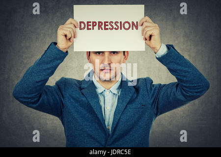 Gestressten Geschäftsmann hält ein Weißbuch über seinen Kopf mit Depression Text geschrieben, auf graue Wand Hintergrund isoliert. Stockfoto