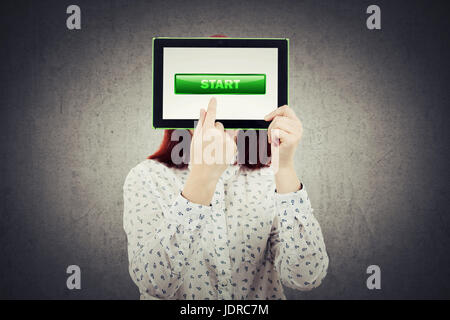 Junge Geschäftsfrau bedeckte ihr Gesicht mit einem digitalen Tablet zeigen ihre Finger auf dem Bildschirm mit einem grünen Startsymbol auf dem Display. Existenzgründung Stockfoto