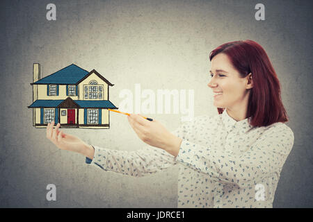 Lächelnde Mädchen zeichnen ein Einfamilienhaus in der Hand. Schutz und Proprety Versicherung Wohnkonzept auf graue Wand Hintergrund isoliert. Stockfoto