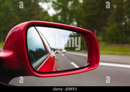 Blick zurück zur Straße durch rote Außenspiegel am Auto Stockfoto