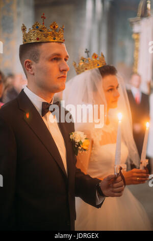 Das Brautpaar mit goldenen Krone auf dem Kopf halten die Kerzen während ihrer Trauung in der Kirche Stockfoto