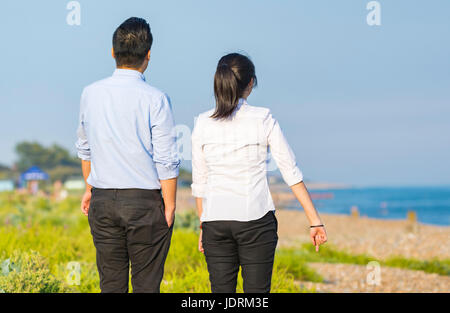 Junge asiatische paar gekleidet intelligent zu Fuß am Strand an einem lauen Sommerabend im Vereinigten Königreich. Stockfoto