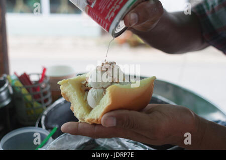 Saler schöpfen Kokosnuss Eis mit Erdnuss und Milch Dressing auf Brot gekrönt. Traditionelle Kokosnusseis in Thailand Stockfoto