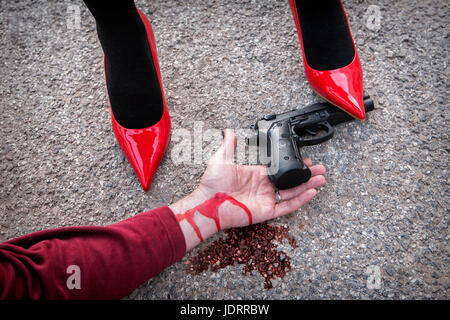 Mann wird dominiert von einer Frau mit roten Schuhen, der Schuh Profiltiefe Pistole Arm blutverschmiert auf dem asphalt Stockfoto