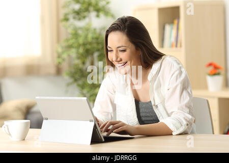 Lässige glückliche Frau e Mail in einem TabletPC auf Linie sitzen in einem Schreibtisch zu Hause mit einem heimeligen Hintergrund schreiben Stockfoto