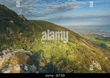 Eine grasbewachsene Bergweg mit blauem Himmel und Wolken drüber. Stockfoto