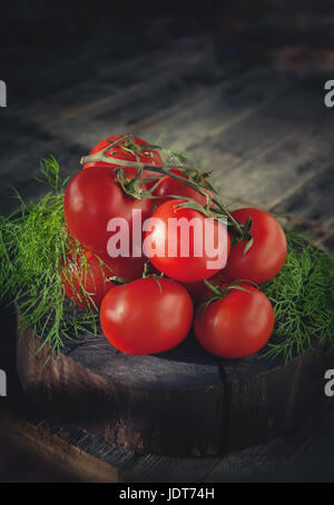 Reife rote Tomaten auf einem Zweig mit grünen frischen Dill liegen auf einem hölzernen Hintergrund im rustikalen Stil. Stockfoto