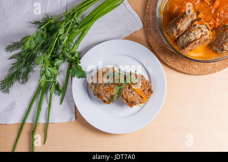 Frikadelle aus Schweinefleisch serviert auf einem weißen Teller und Kräuter - Dill, Frühlingszwiebeln, Petersilie um die Platte. Hausgemachte Frikadellen, gebraten mit Gemüse in Keramik Stockfoto