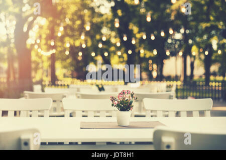 romantisches Gartenrestaurant im Park mit Lichterketten bei Sonnenuntergang Stockfoto