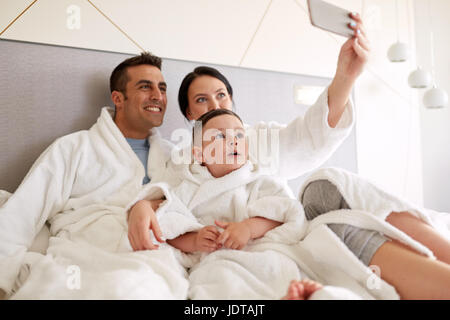 glückliche Familie mit Smartphone im Bett im Hotelzimmer Stockfoto