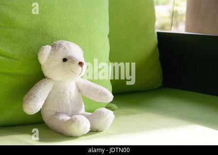 Smilely Weißer Teddybär auf Sofa sitzen und liegen auf grünen Kissen Stockfoto