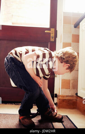 Junge, seine Schuhe zu binden, an Tür Stockfoto