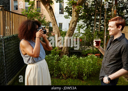 Junge Frau, die Mann im Garten fotografieren Stockfoto