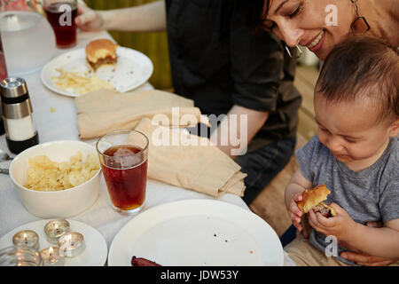 Mutter hält Baby Boy am Tisch im Garten-Partei, Lächeln Stockfoto