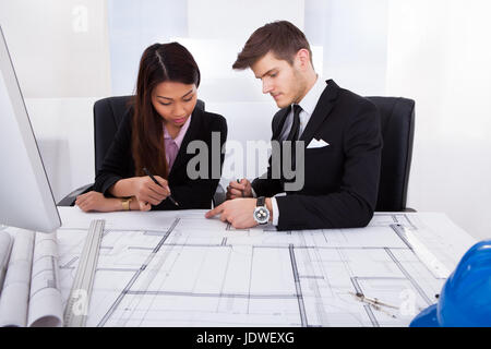 Junge Architekten arbeiten gemeinsam an Blaupause am Schreibtisch im Büro Stockfoto